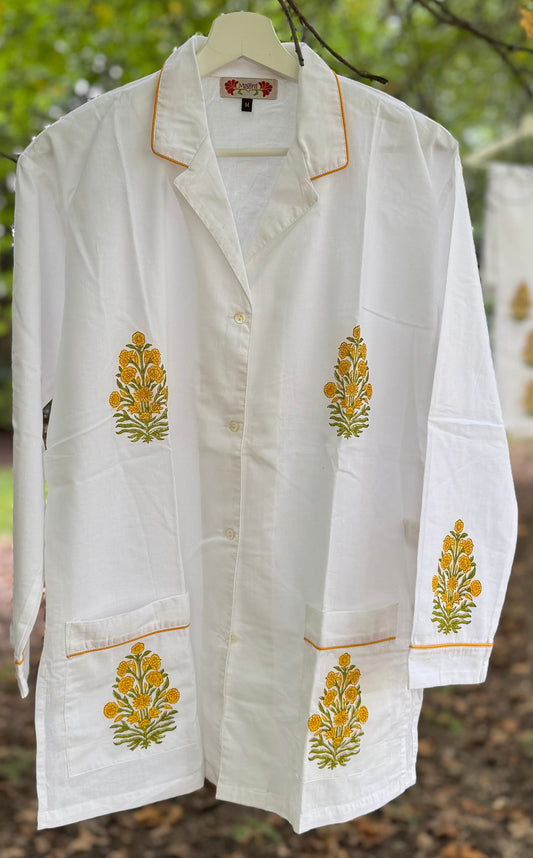 Pigiama due pezzi in cotone voile bianco con stampe floreali Buti ocra fatte a mano, appeso tra rami verdi in un contesto naturale.