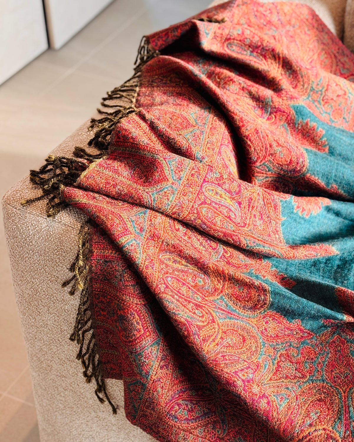 Coperta paisley rossa e verde petrolio appoggiata sul bracciolo del divano
