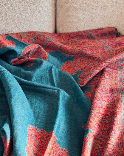 Coperta in lana verde petrolio aperta sul divano, bordo paisley rosso