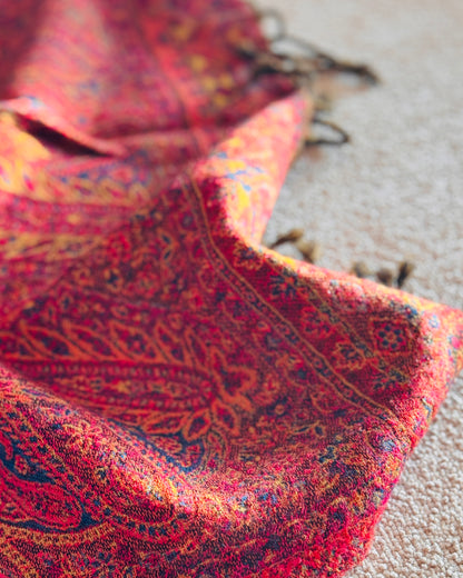 Coperta paisley rossa aperta sul divano, con frange