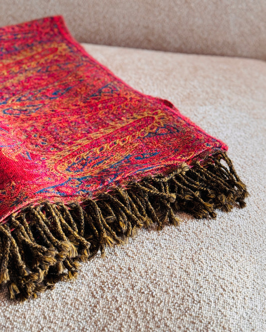 Coperta paisley rossa piegata, dettaglio delle frange marrone e oro