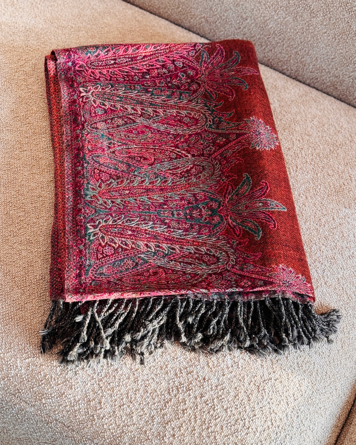 Coperta in lana jacquard arancio rame con paisley fucsia piegata sul divano, con frange