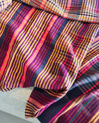 Plaid tartan in lana merino aperto sul divano, righe magenta e senape
