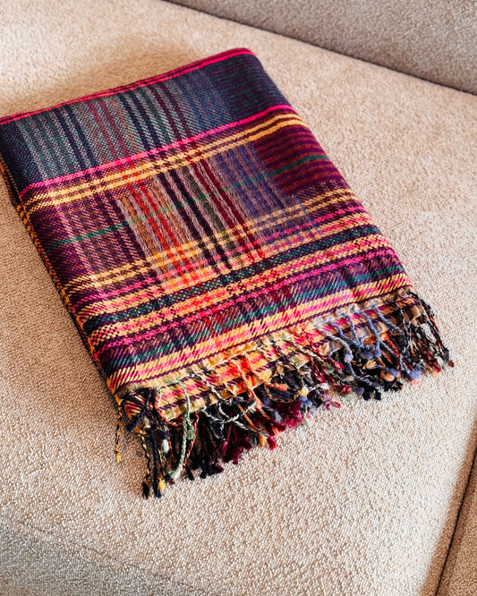 Plaid in lana merino tartan magenta, viola e senape piegato sul divano, con frange