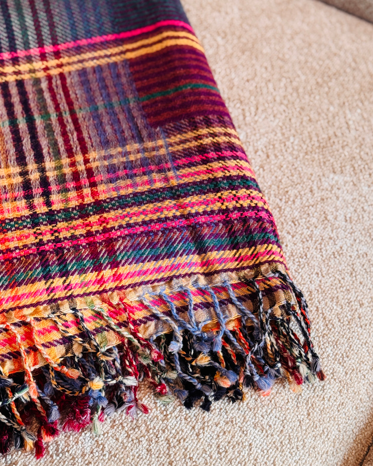 Dettaglio delle frange ritorte e della trama tartan magenta e senape