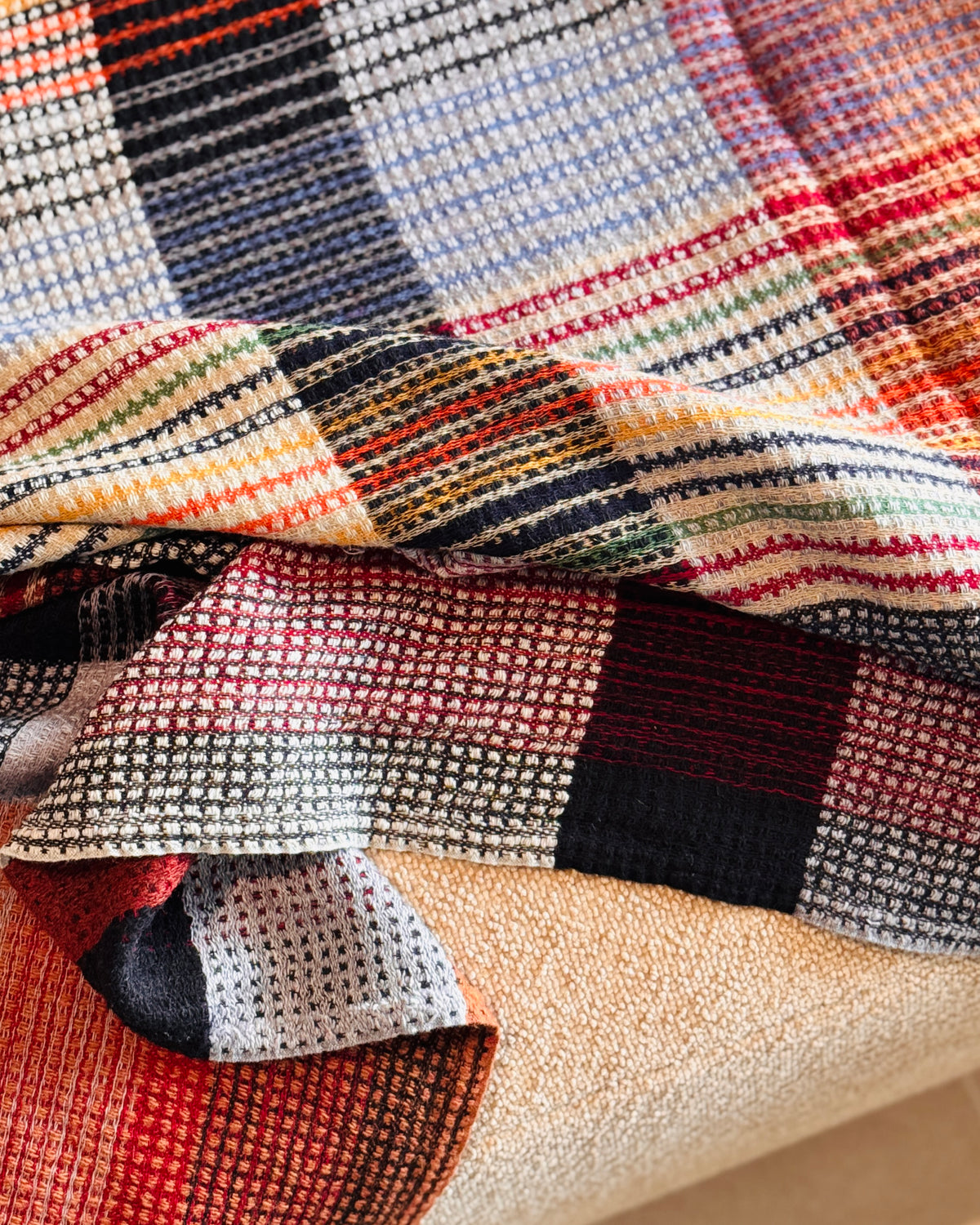 Plaid a quadri blu, nero e grigio piegato sul divano, trama in rilievo