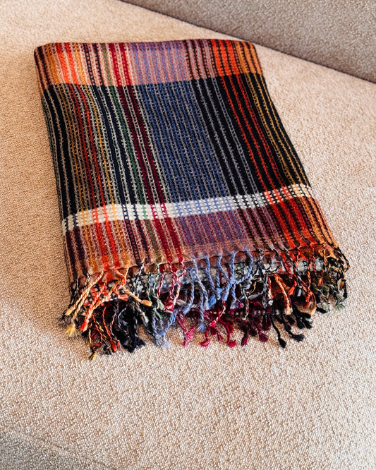 Plaid in lana merino a quadri blu e arancio piegato sul divano, con frange