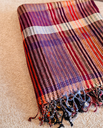 Plaid a quadri viola, rosso e arancio piegato, con frange multicolore