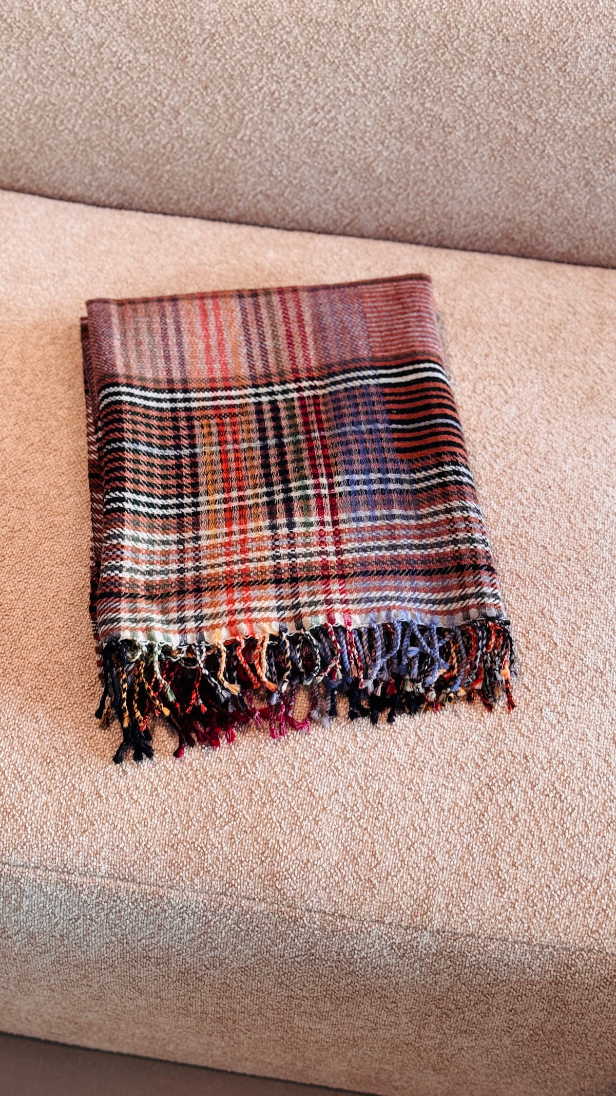 Plaid in lana merino tartan rosso mattone e arancio piegato sul divano, con frange