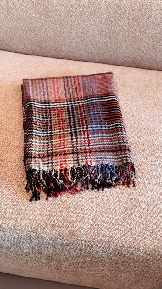 Plaid in lana merino tartan rosso mattone e arancio piegato sul divano, con frange