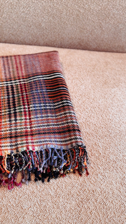 Plaid tartan rosso mattone piegato, dettaglio delle frange multicolore