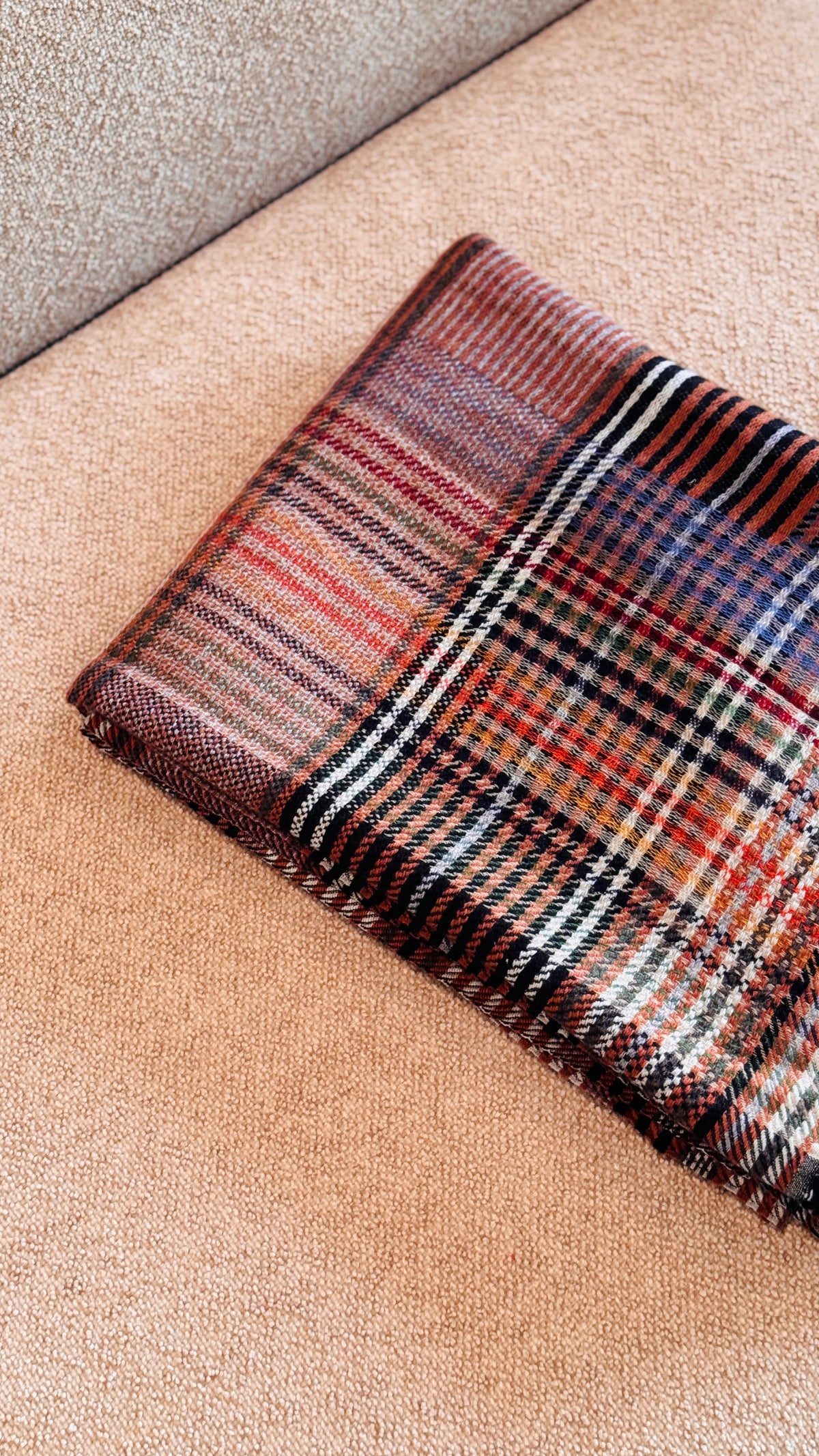 Bordo del plaid tartan piegato, righe crema, nere e lavanda su fondo rosso mattone