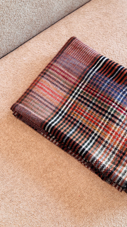 Bordo del plaid tartan piegato, righe crema, nere e lavanda su fondo rosso mattone