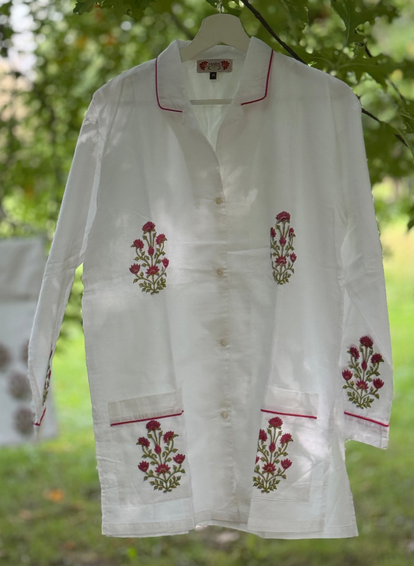 Set pigiama in cotone voile bianco con stampe Buti rosse block print, camicia con piping rosso e pantalone coordinato appesi in giardino.