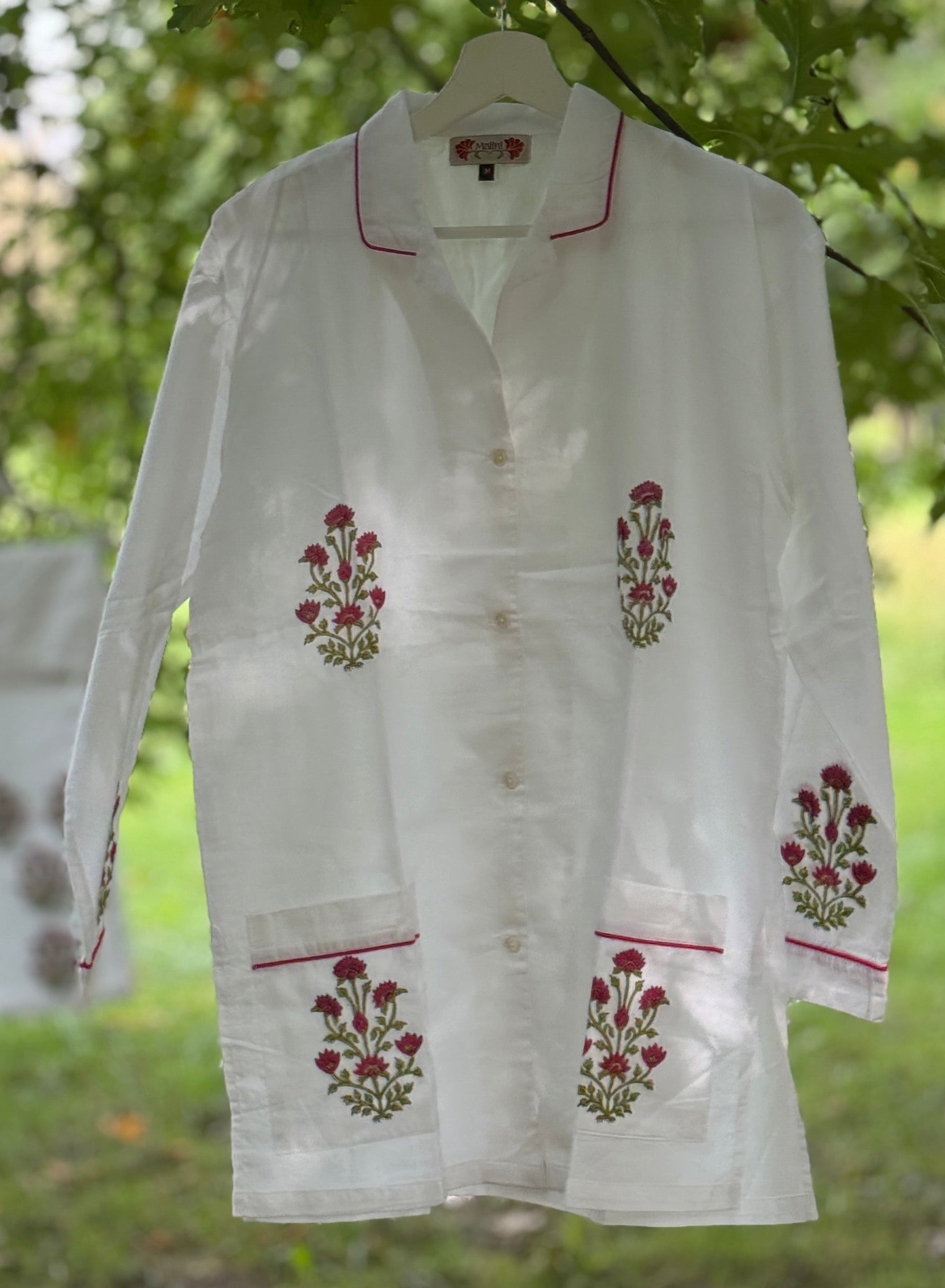 Set pigiama in cotone voile bianco con stampe Buti rosse block print, camicia con piping rosso e pantalone coordinato appesi in giardino.